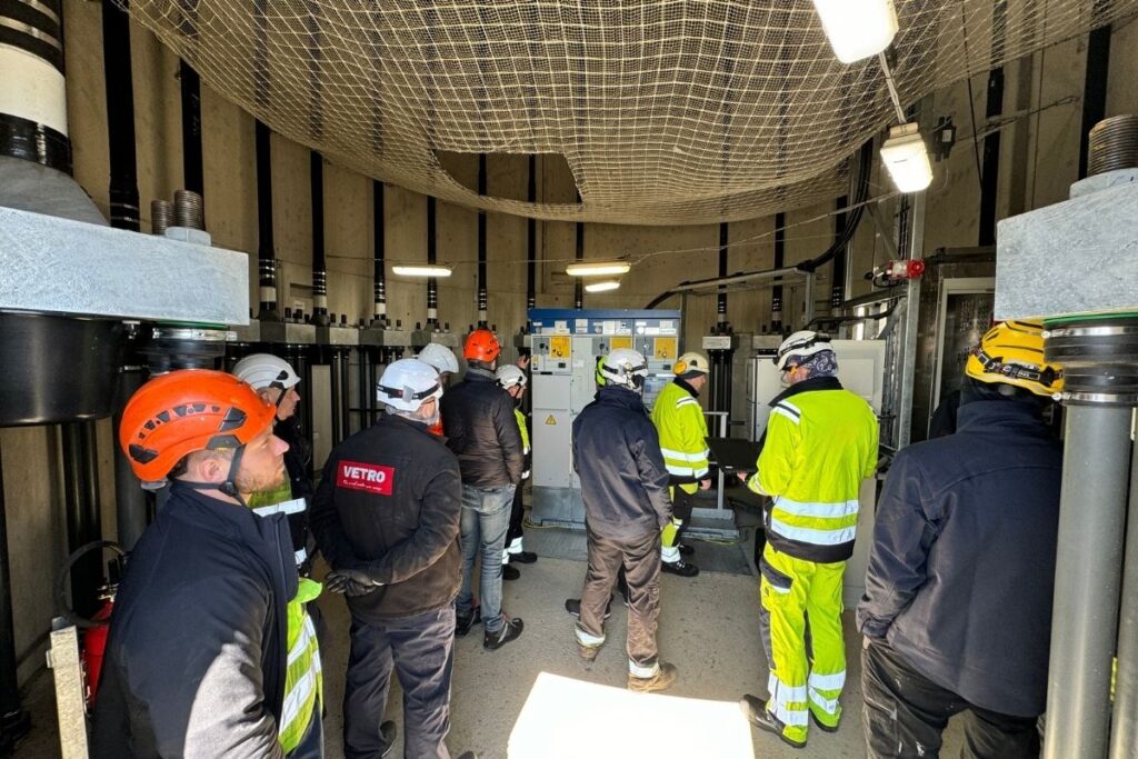 Techniker mit Schutzhelmen und Warnkleidung an elektrischen Schaltanlagen