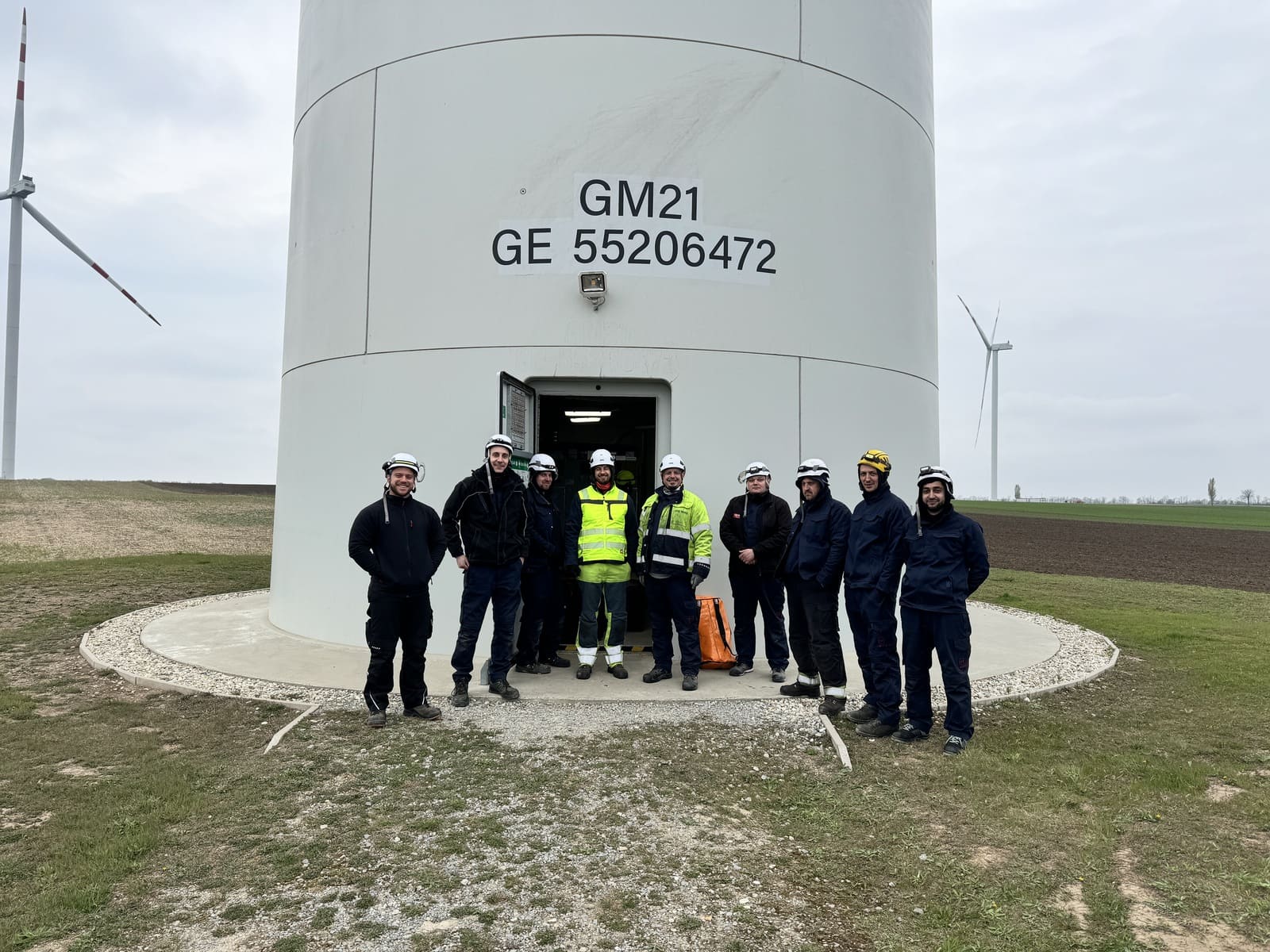 Technikerteam mit Schutzhelmen vor dem Turmfuß einer Windenergieanlage