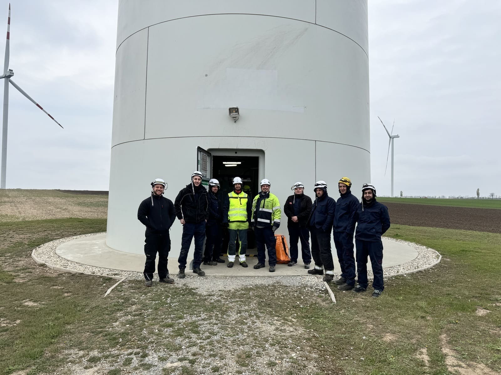 Technikerteam mit Schutzhelmen vor dem Turmfuß einer Windenergieanlage