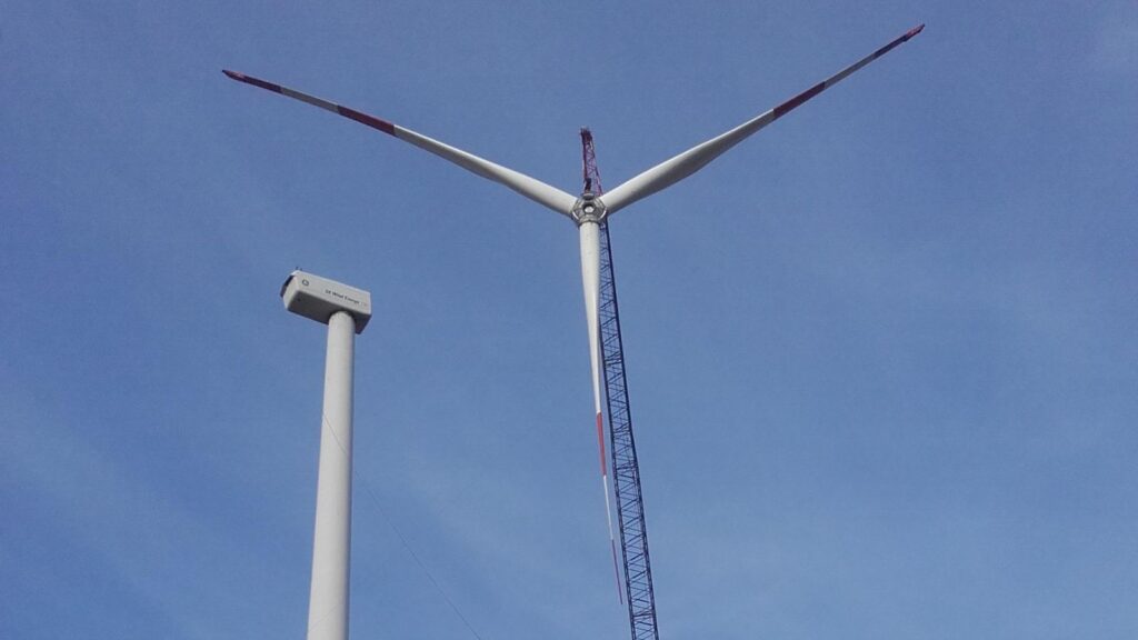 Windenergieanlage neben einem Turm ohne Rotorblätter während Kranarbeiten